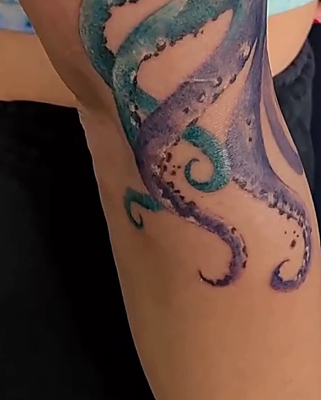 Tentáculos de pulpo en azul y morado que tapan un tatuaje anterior, en el brazo