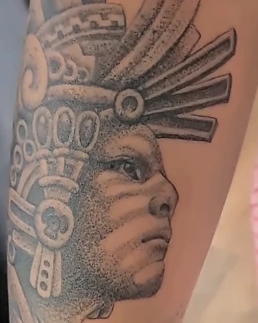 Retrato de guerrero mexica con penacho en puntillismo negro y gris, en el antebrazo